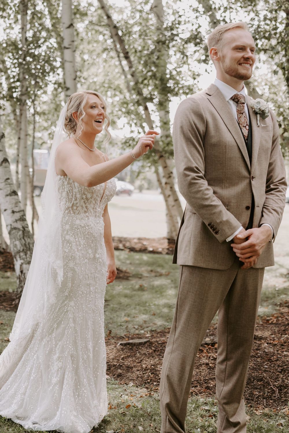 Bride laughing joyfully as groom smiles during their first look among birch trees.
