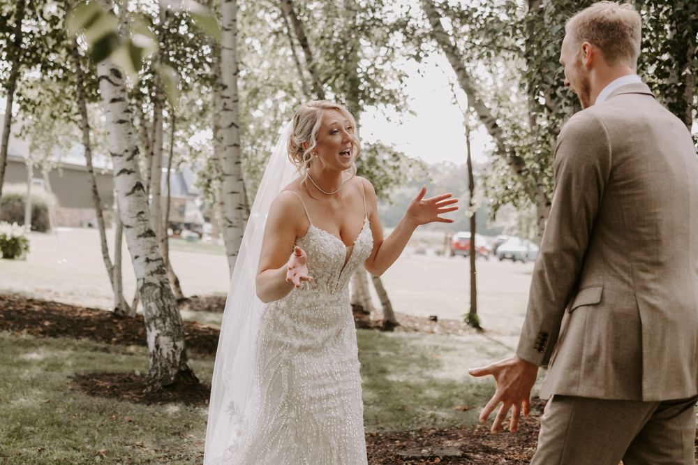 Bride and groom sharing an emotional first look reaction outdoors among birch trees.