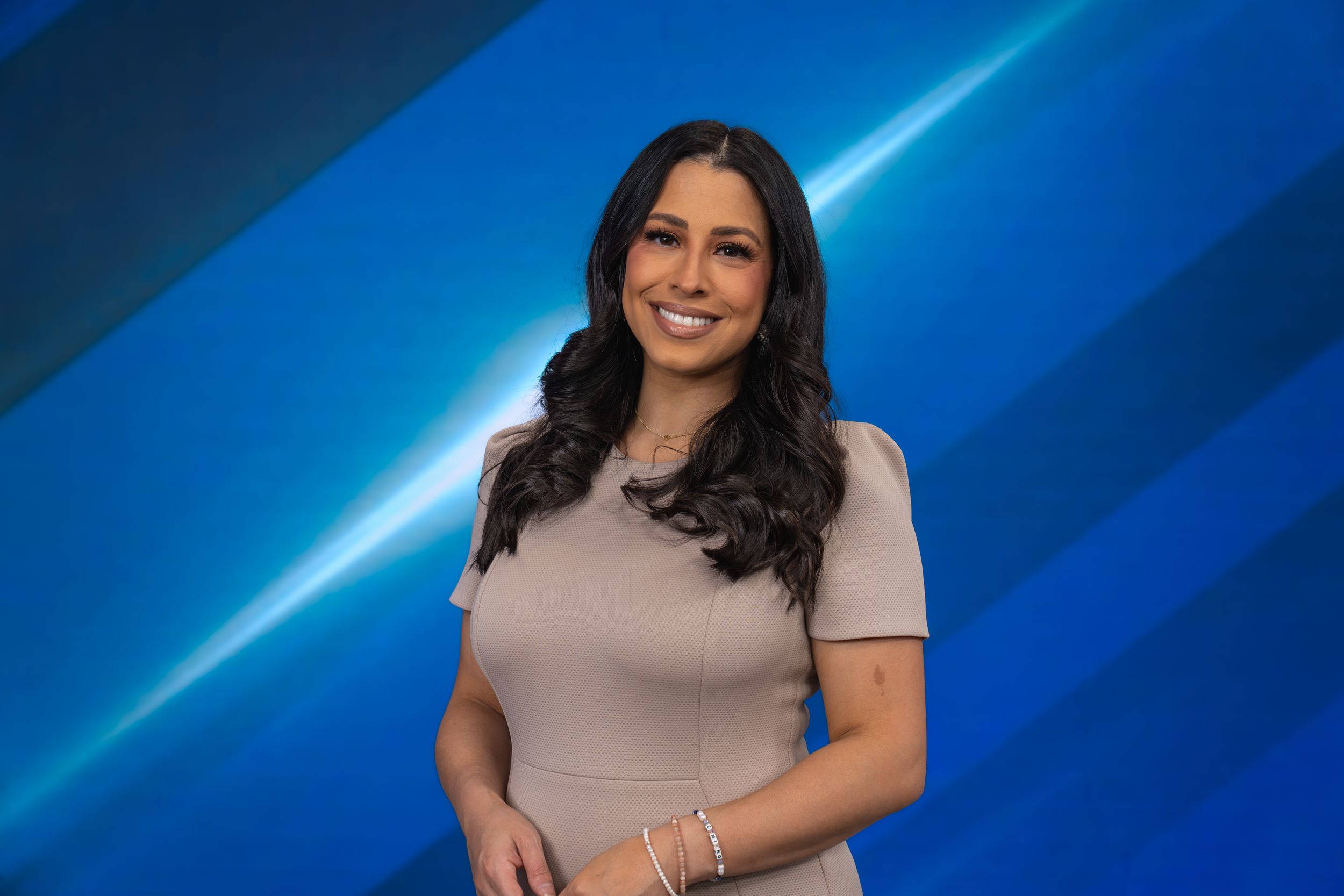 Professional woman in beige dress smiling confidently against a blue studio background.