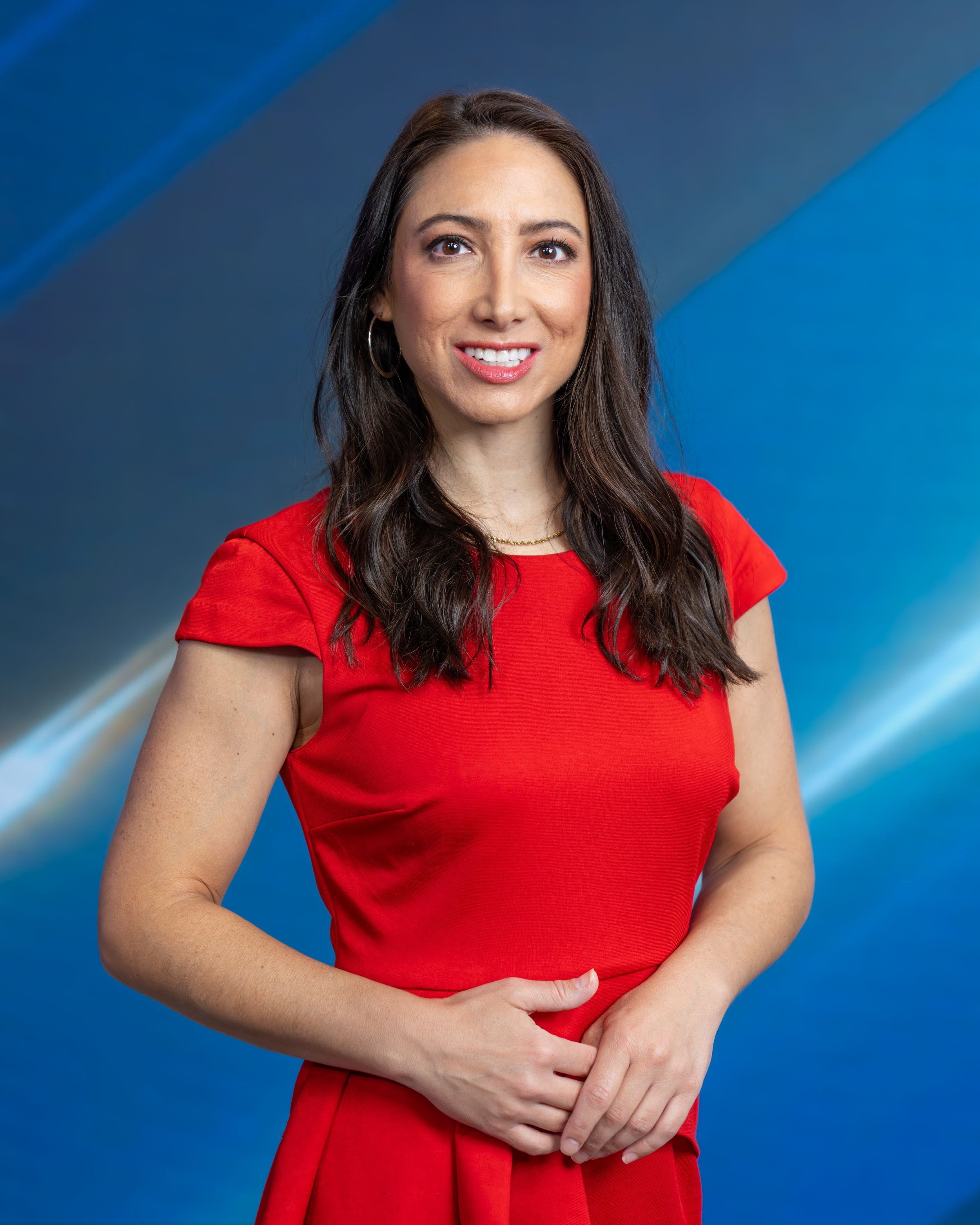Professional headshot portrait of person in red dress against blue gradient background.