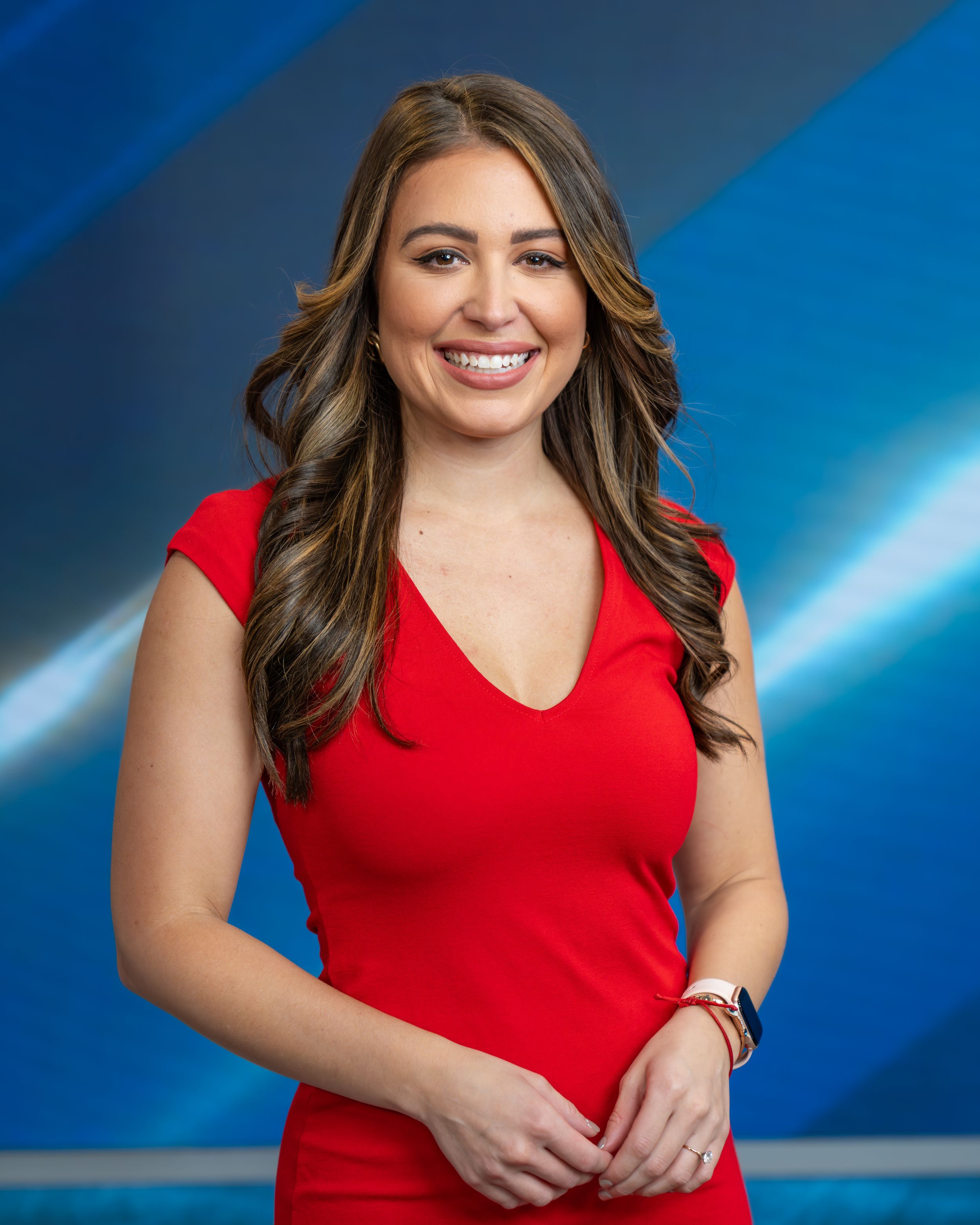 Professional headshot portrait of a person in a red v-neck dress against a blue gradient background.