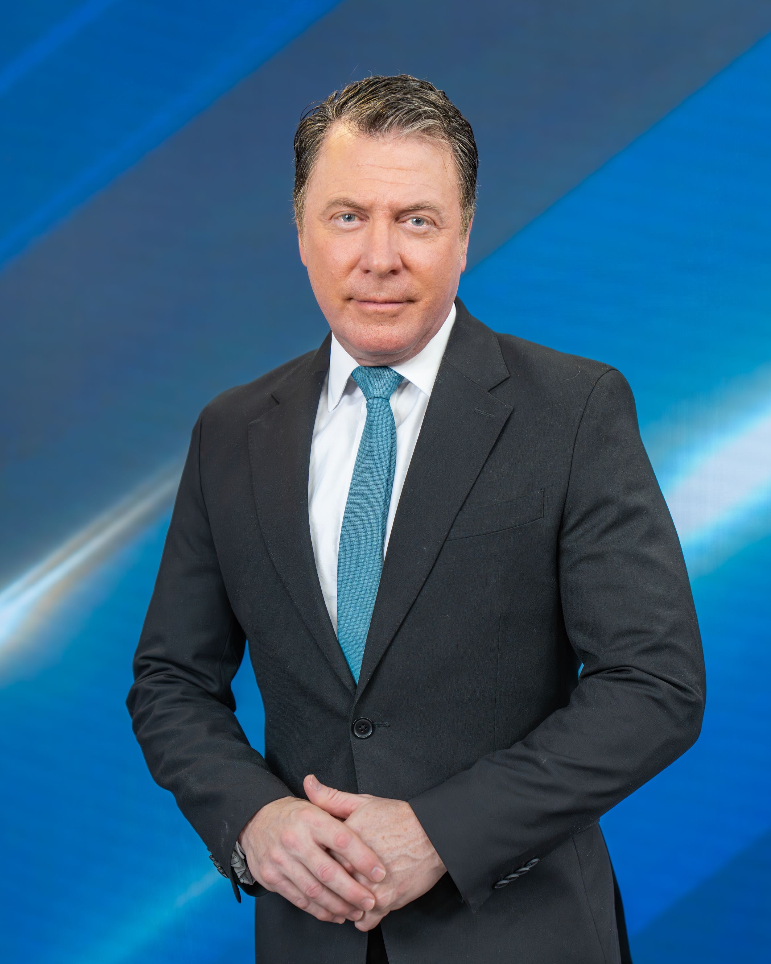 Professional headshot of a person in a dark suit and blue tie against a blue gradient background.