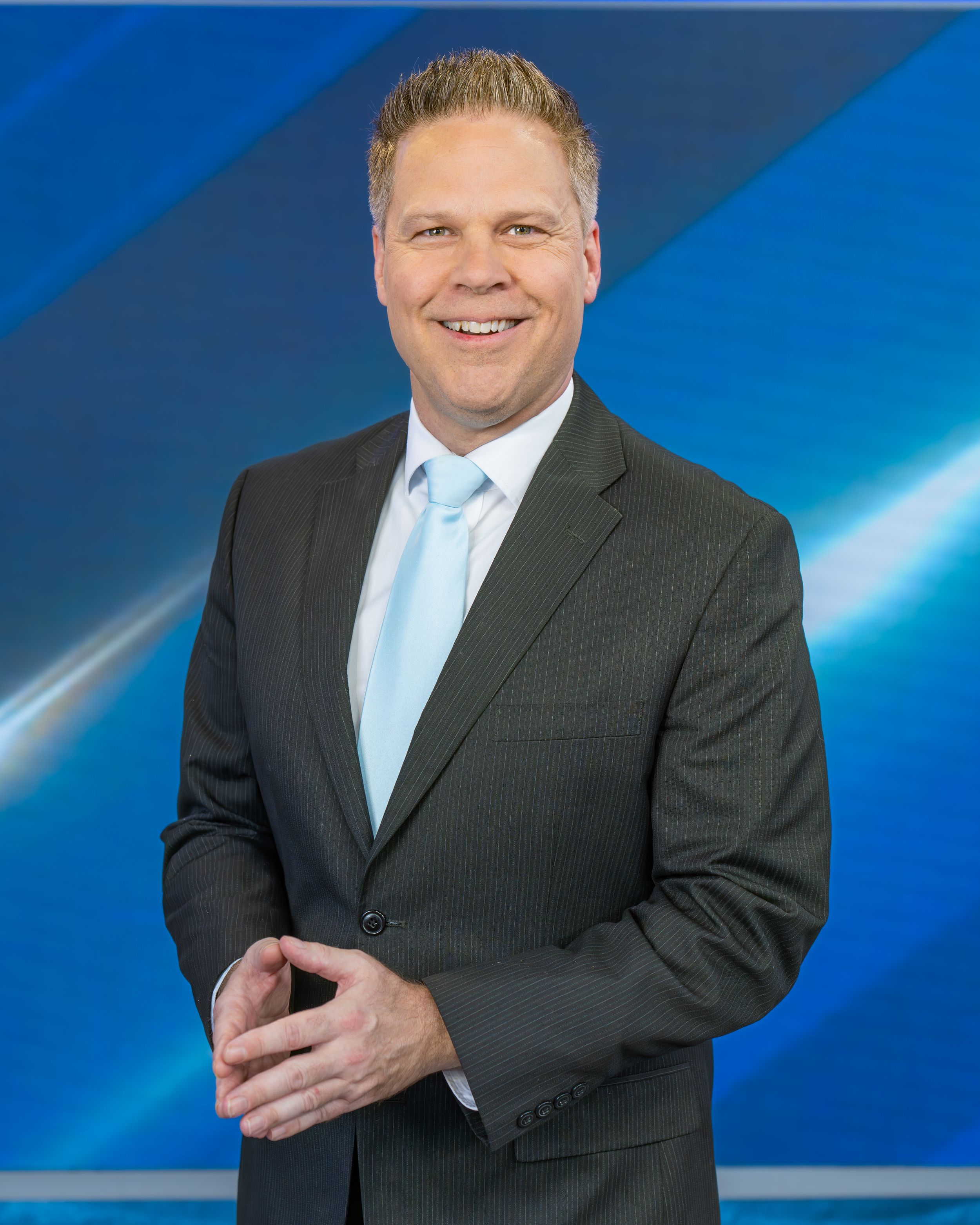 Professional in dark suit and light blue tie poses against blue backdrop in series of headshots.