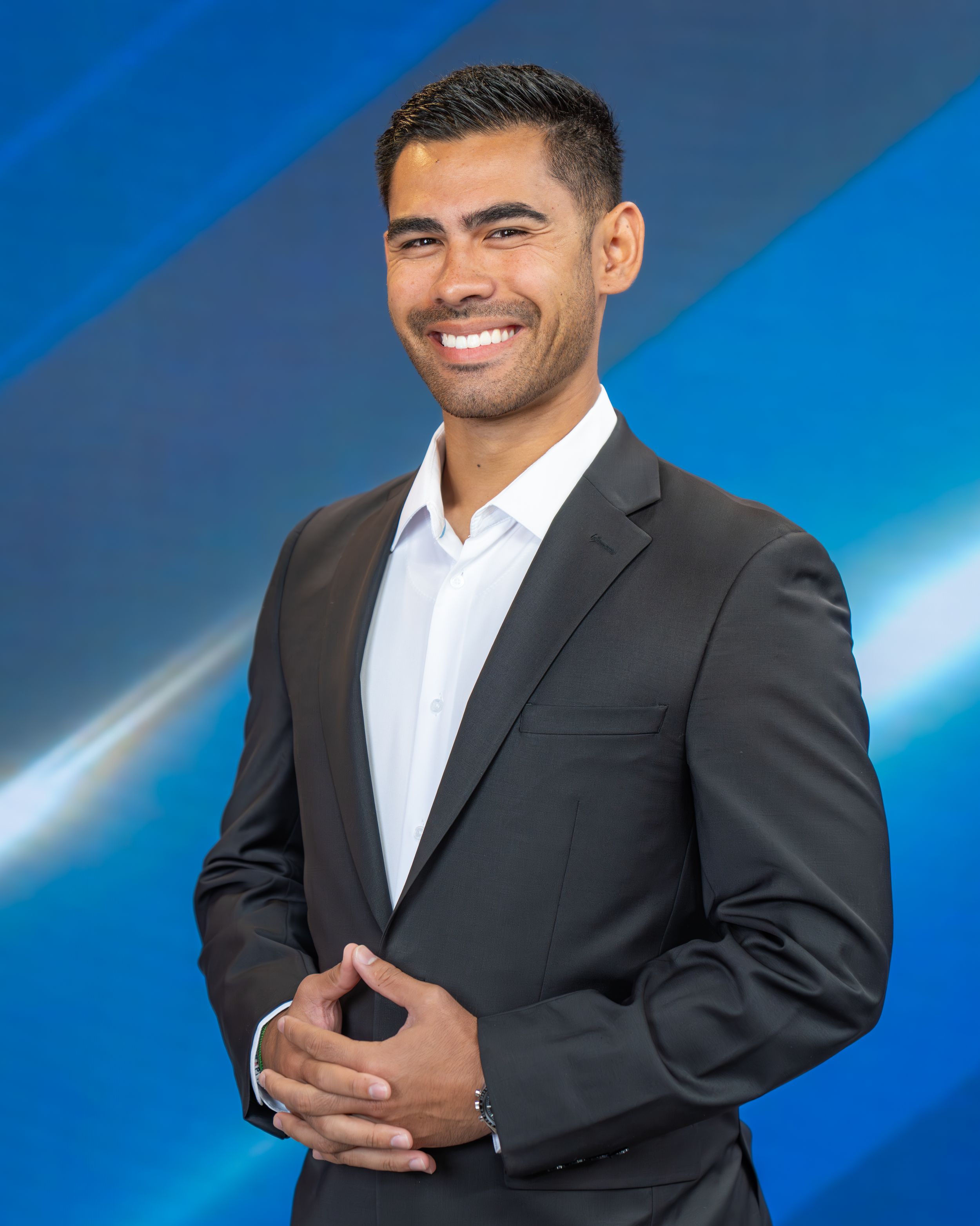 Professional headshot of someone in a black suit and white dress shirt against a blue gradient background.