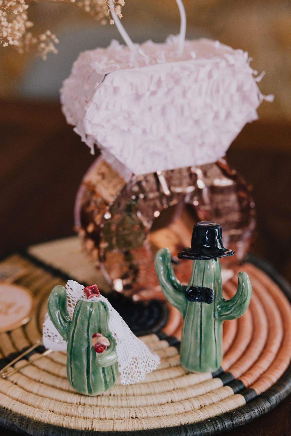 Ceramic cactus bride and groom cake toppers displayed with pink pinata and disco ball wedding decor.