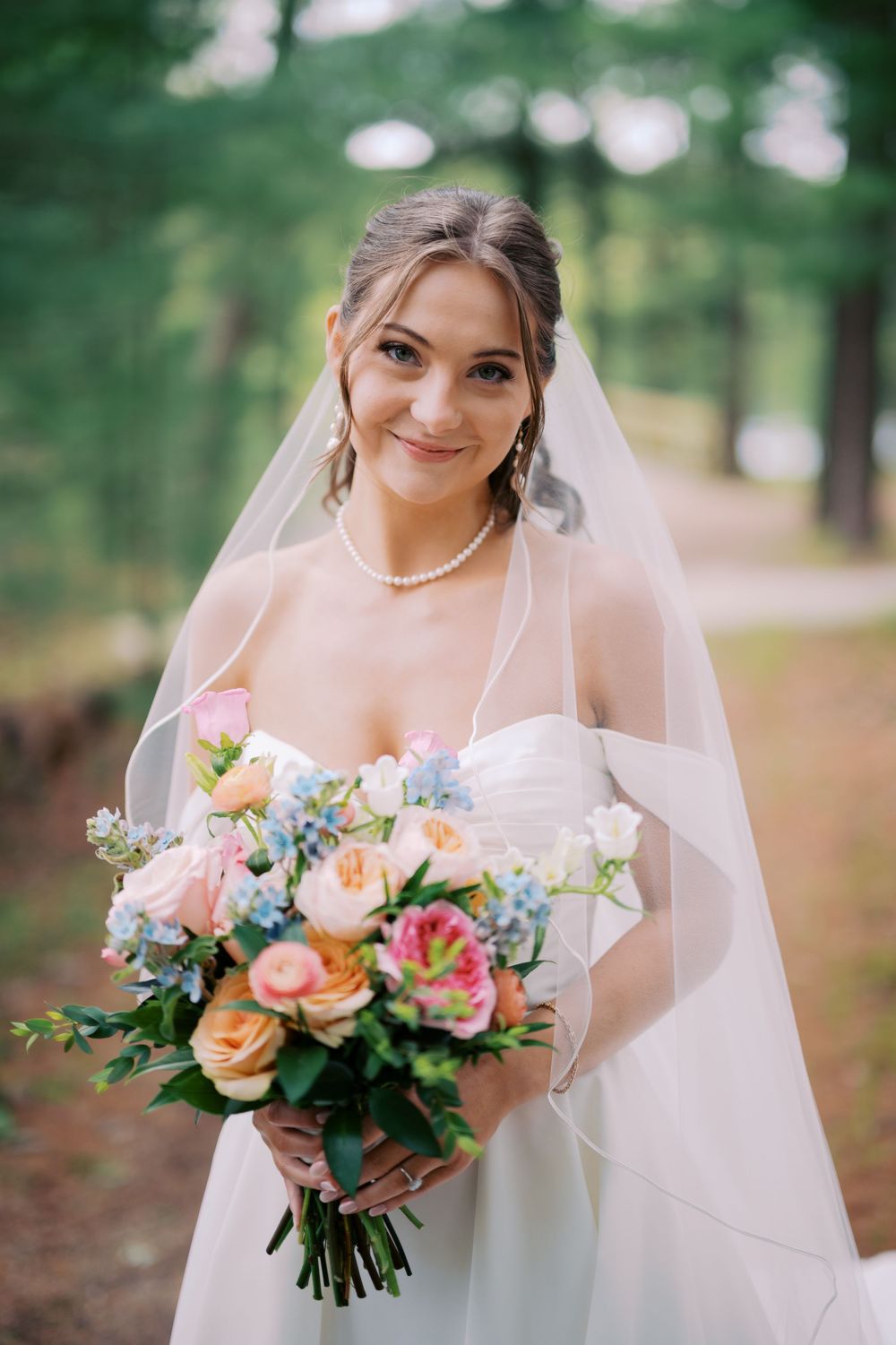 A bridal portrait series showing a white wedding dress, delicate veil, and vibrant peach and pink floral bouquet in a forest setting.