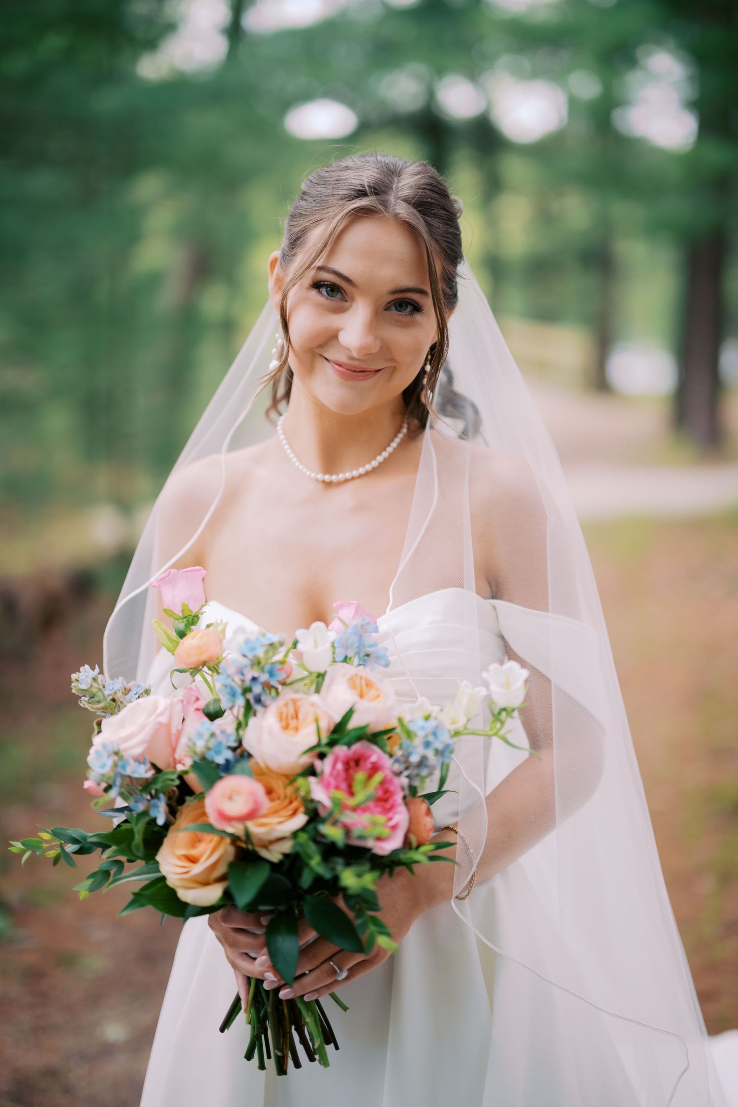 A bridal portrait series showing a white wedding dress, delicate veil, and vibrant peach and pink floral bouquet in a forest setting.