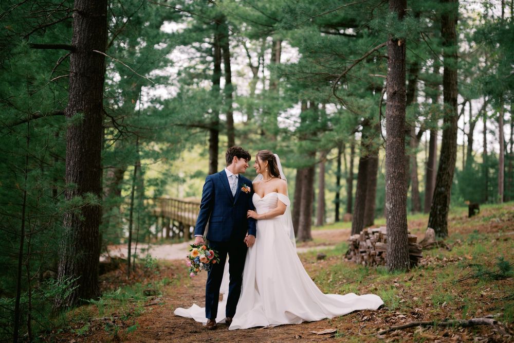 A couple in wedding attire poses together in a serene pine forest setting during their special day.