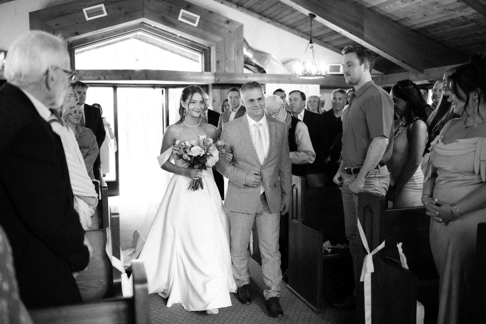 Wedding party celebrates and dances together on a rustic wooden dance floor during an indoor reception.