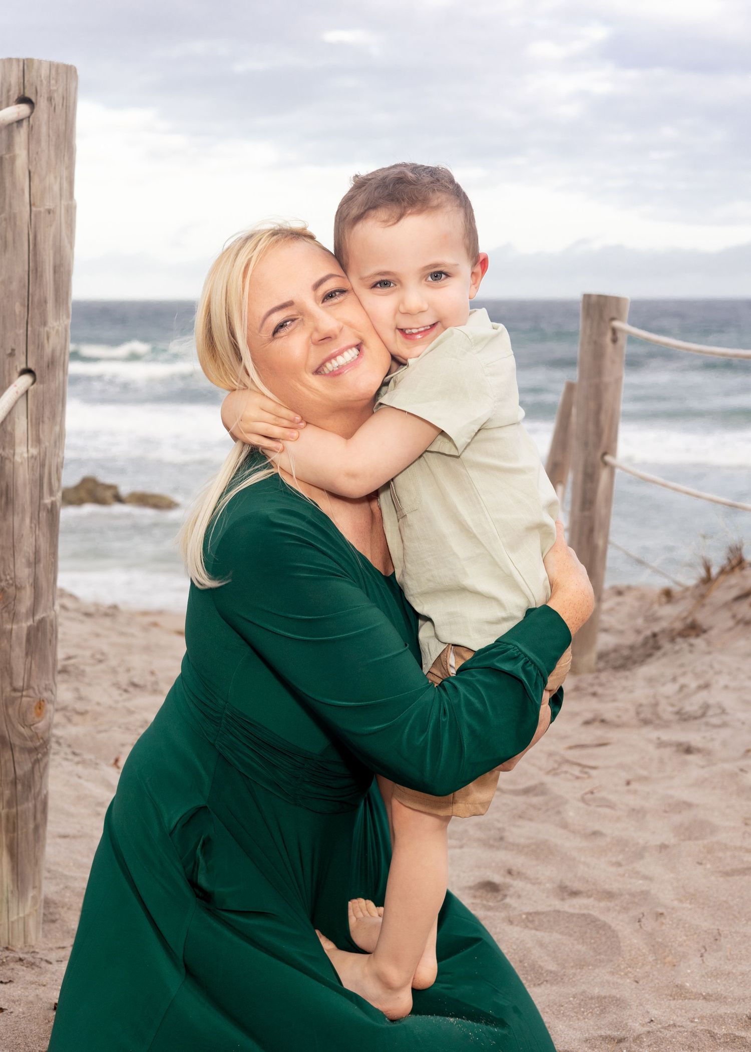 A loving moment shared between two people at a beach with wooden posts and waves in the background.