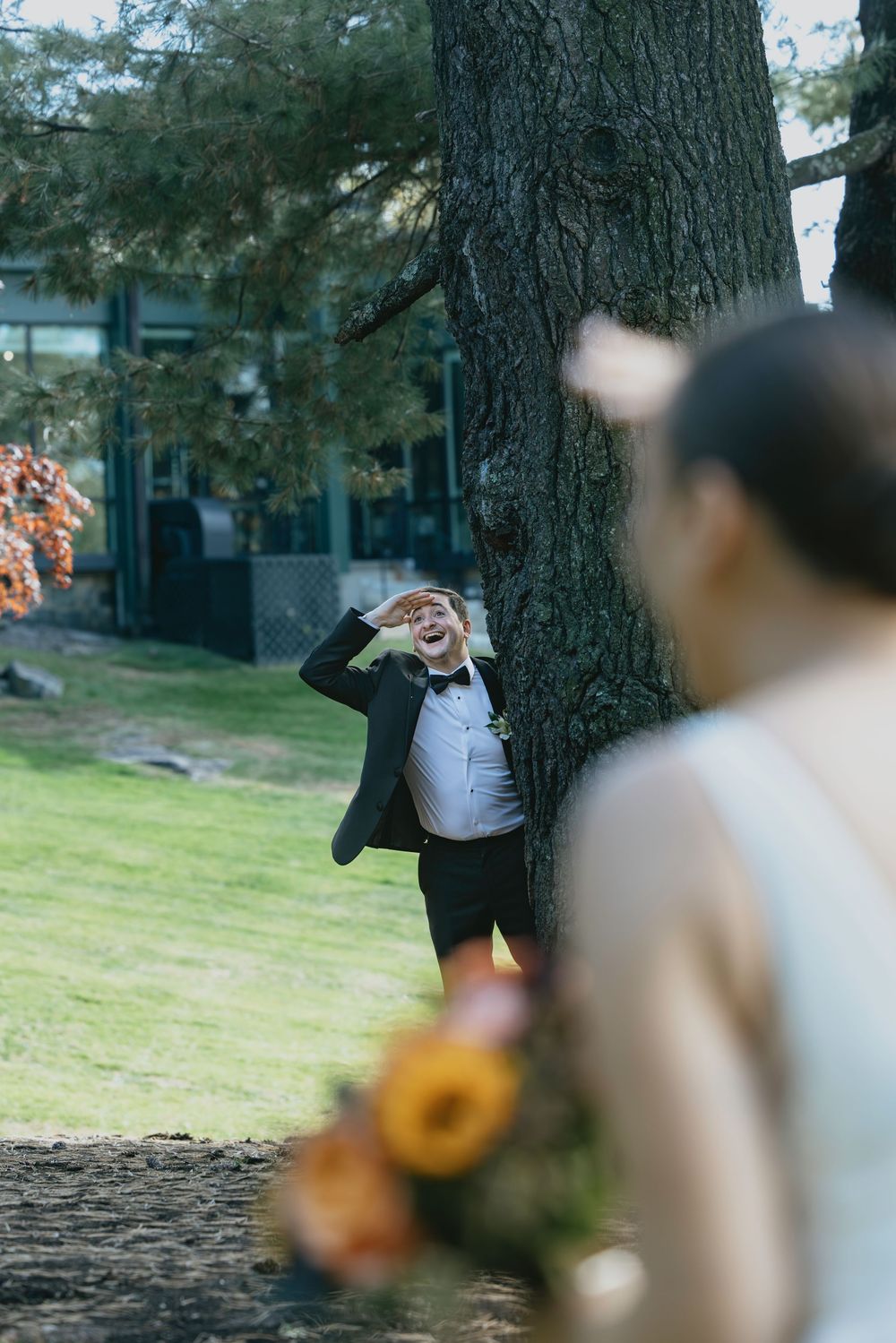 A playful wedding photo shoot moment by a large tree trunk in a garden setting.