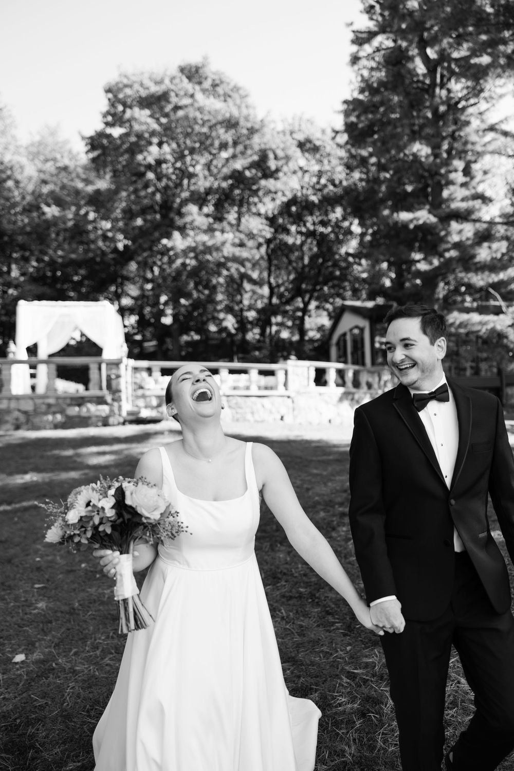 A joyful couple shares a candid laughing moment together in their wedding attire outdoors.