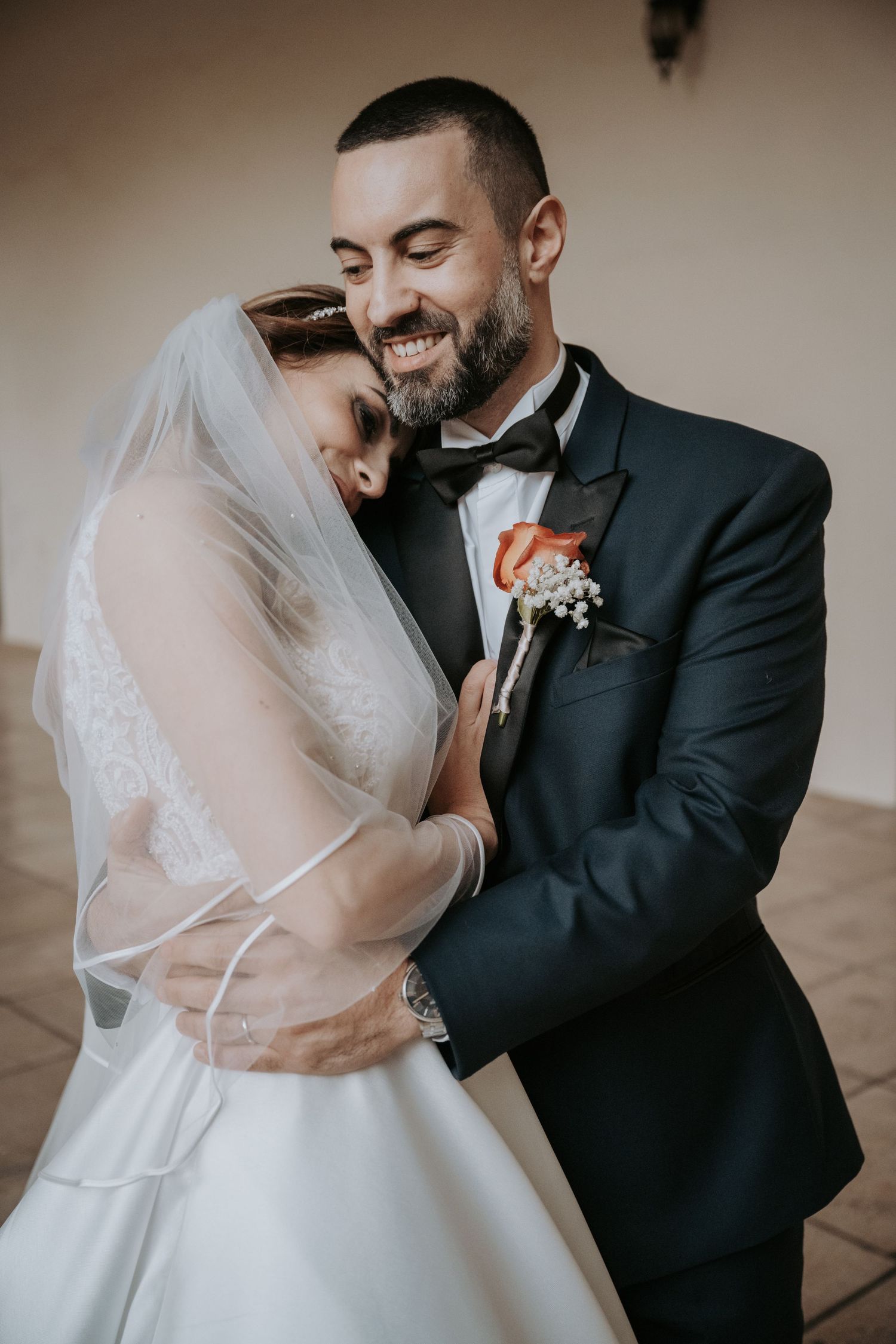 A tender wedding moment captured as newlyweds embrace, with the bride in white and groom in classic black tuxedo.