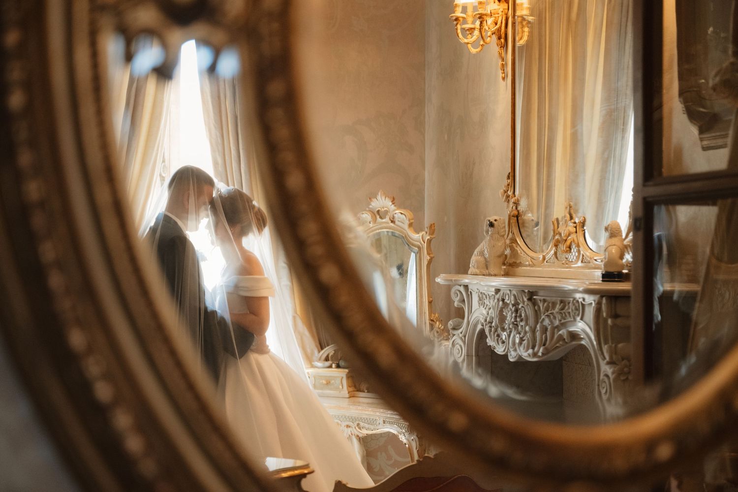 Vintage ornate gold mirror reflects sunlight streaming through window in elegant room with antique decor.