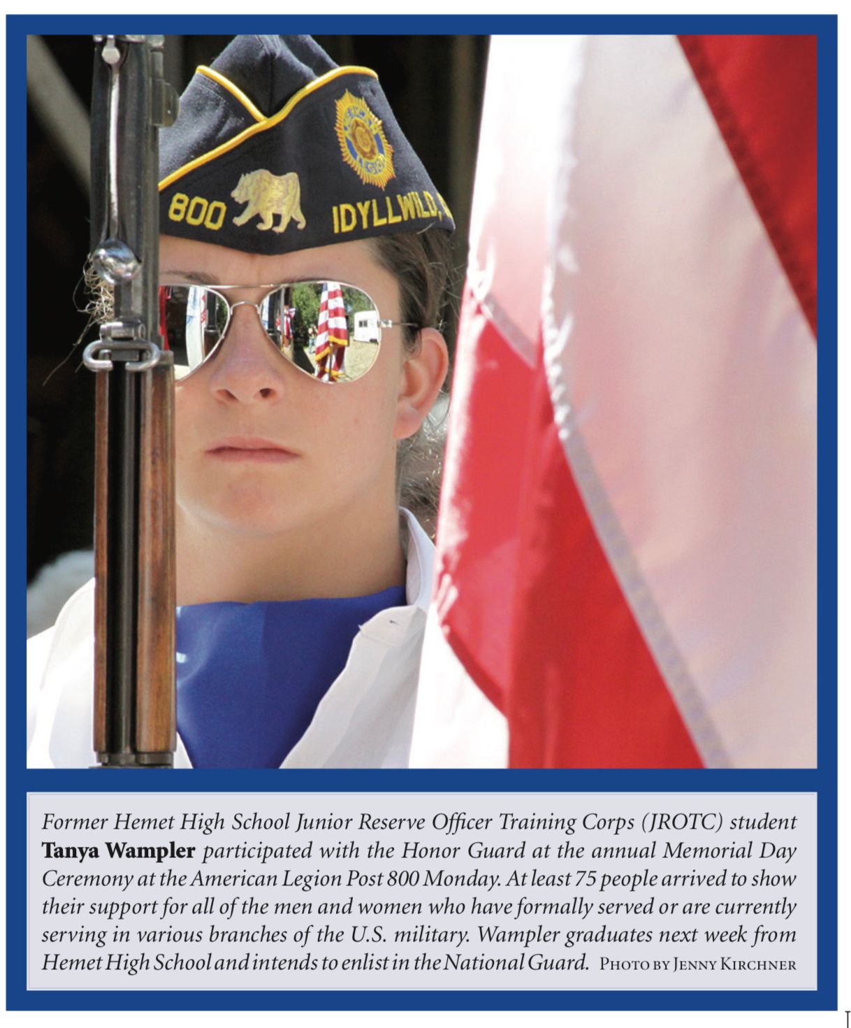A student in a military uniform and sunglasses stands with American flags in the background during a ceremony.