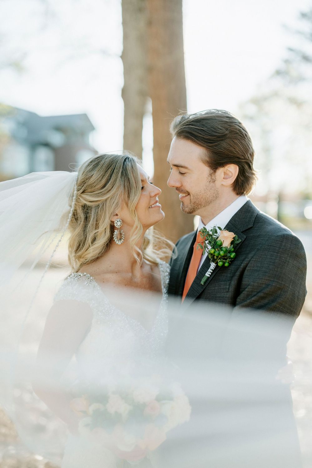 Romantic wedding couple sharing an intimate moment in soft sunlight with a flowing veil creating a dreamy atmosphere.