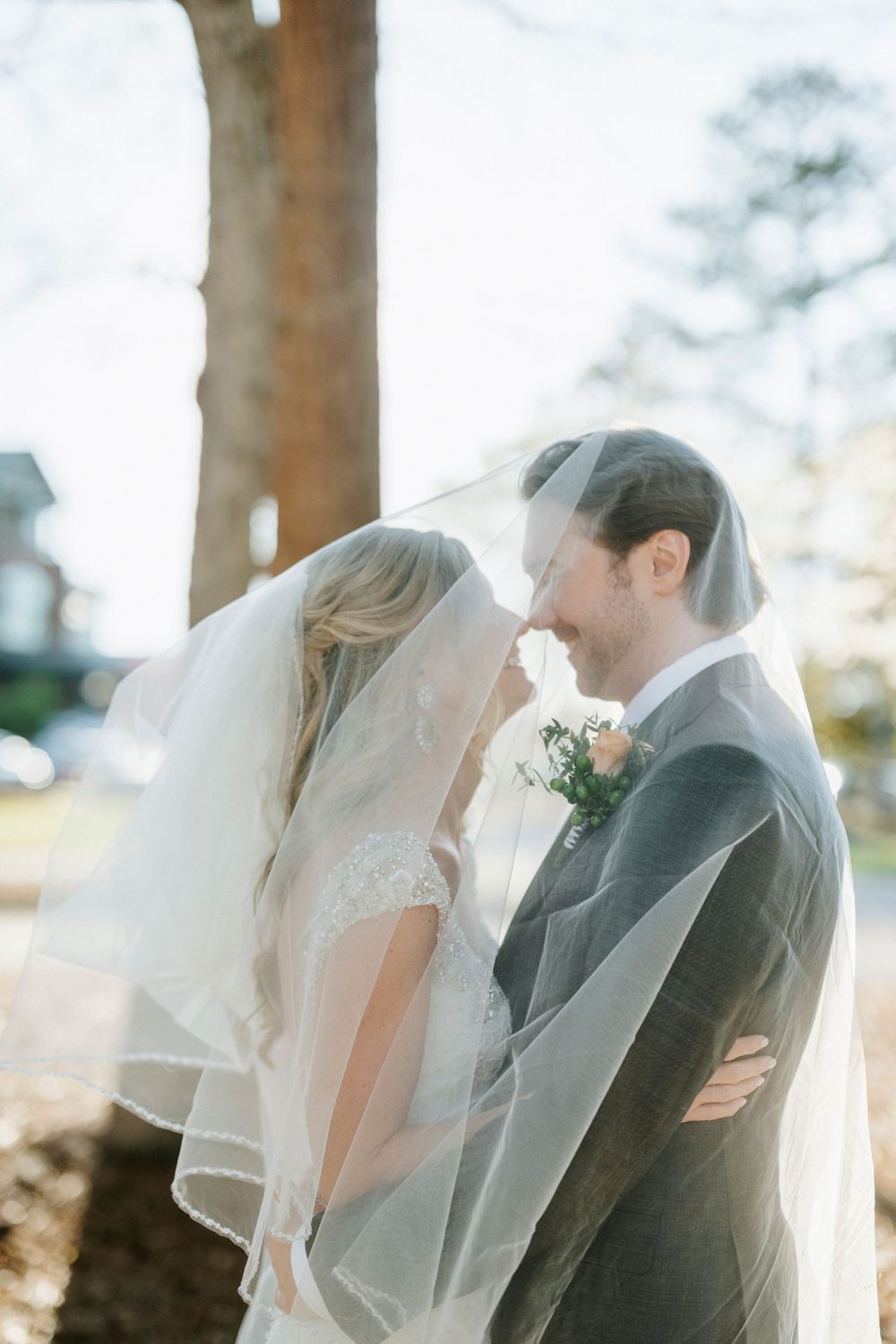 Romantic outdoor wedding moment with couple sharing an intimate kiss under a flowing veil on a sunny day.