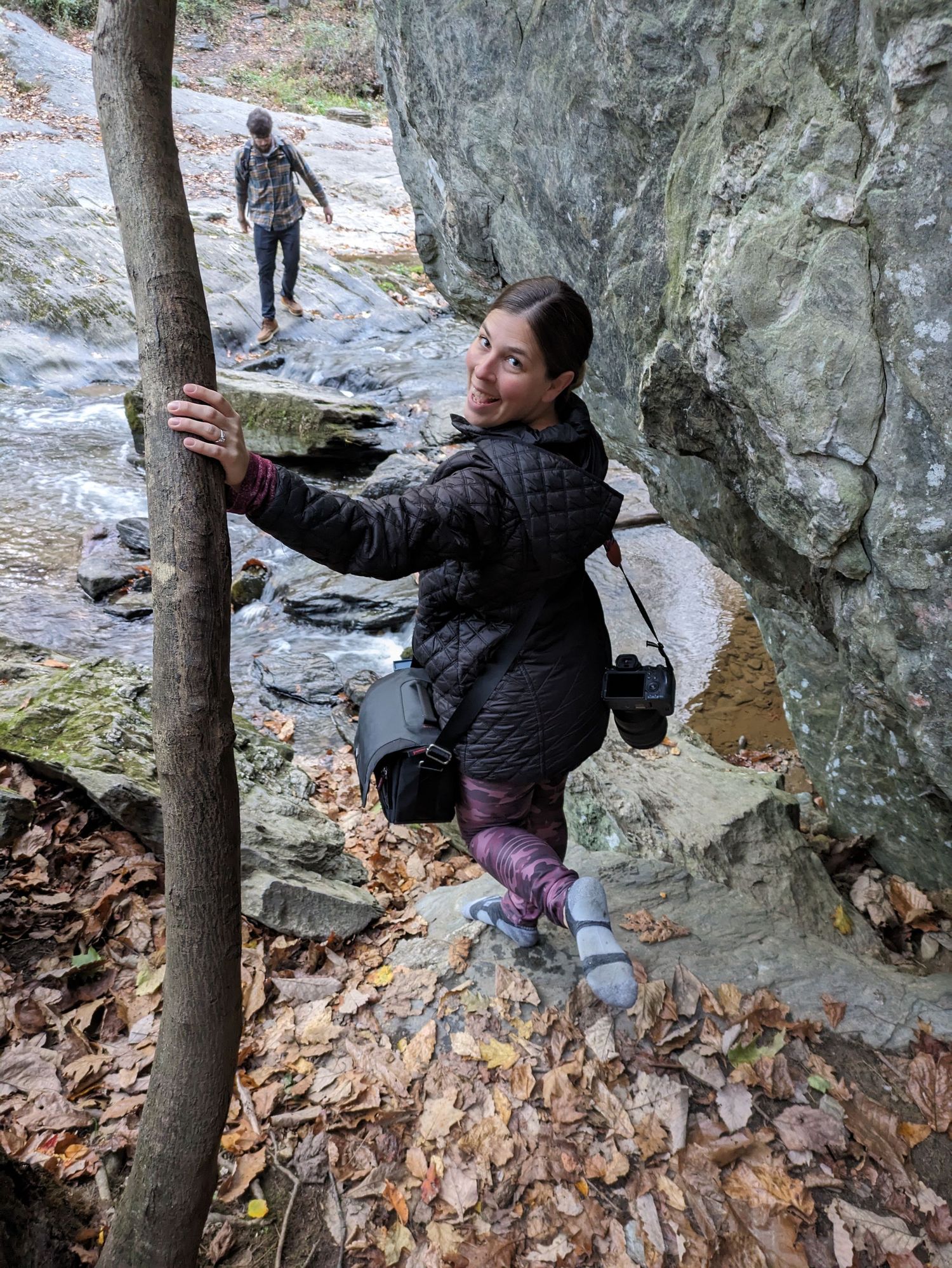 Rock climber navigates a challenging bouldering route on a rocky cliff face covered in fallen autumn leaves.
