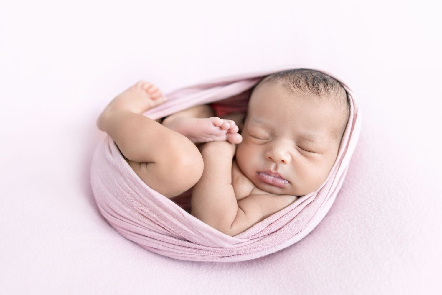 A collage of four peaceful newborn baby photos with soft pink fabric and delicate lighting effects.
