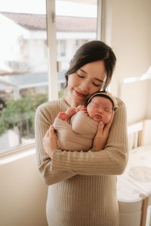 Tender moment with baby wrapped in beige knit sweater by sunlit window.陽光灑在窗邊，嬰兒裹著米色針織毛衣，溫馨的一刻。
