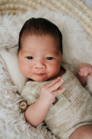 Baby wearing knit sweater lying on textured cream blanket.穿著針織毛衣的嬰兒躺在米色紋理毯子上。