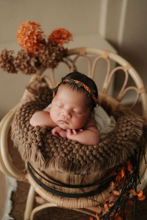 Sleeping newborn rests in brown fur basket with delicate orange floral accents creating a cozy autumn scene熟睡的新生兒躺在棕色毛絨籃子裡，籃子上點綴著精緻的橙色花朵