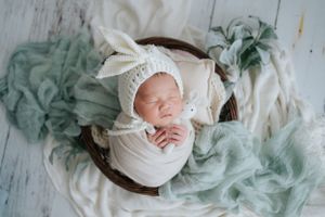 Newborn photography with white wraps and sage green fabric accents以白色襁褓和鼠尾草綠色布料點綴的新生兒攝影。