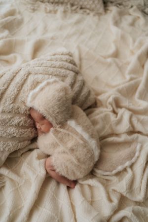 Close-up of tiny baby feet wrapped in soft beige blanket against textured background.特寫鏡頭：裹在柔軟米色毯子裡的嬰兒小腳丫，背景是紋理豐富的圖案。