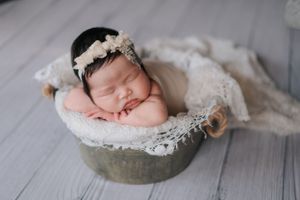 Artistic newborn portrait on gray vintage wooden floor with lace and soft fabric details.在灰色復古木地板上拍攝的藝術感十足的新生兒肖像照，飾以蕾絲和柔軟的布料細節。