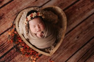 Close-up shot of newborn baby sleeping on rustic wooden backdrop with red berries特寫鏡頭：新生兒睡在質樸的木質背景上，背景點綴著紅色莓果。