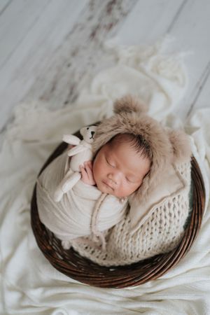 Sleeping newborn wrapped in beige swaddle resting in woven basket.裹在米色襁褓裡的新生兒安睡在編織籃中。