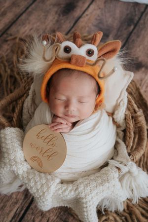 Newborn wearing adorable owl-themed hat sleeps peacefully on white knit blanket.戴著可愛貓頭鷹帽的新生兒在白色針織毯上安然入睡。
