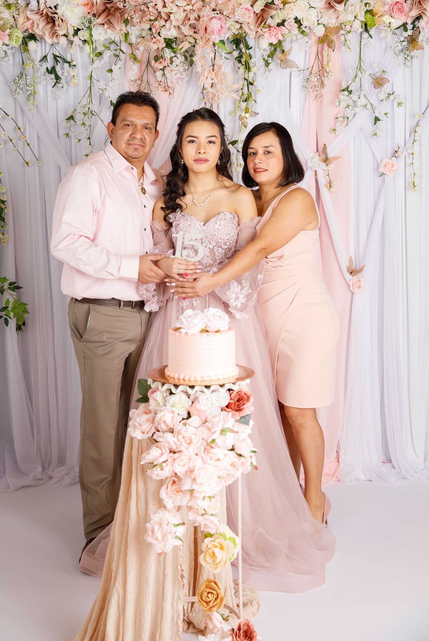 A family celebrates with a beautiful pink floral wedding cake against a romantic flower wall backdrop.