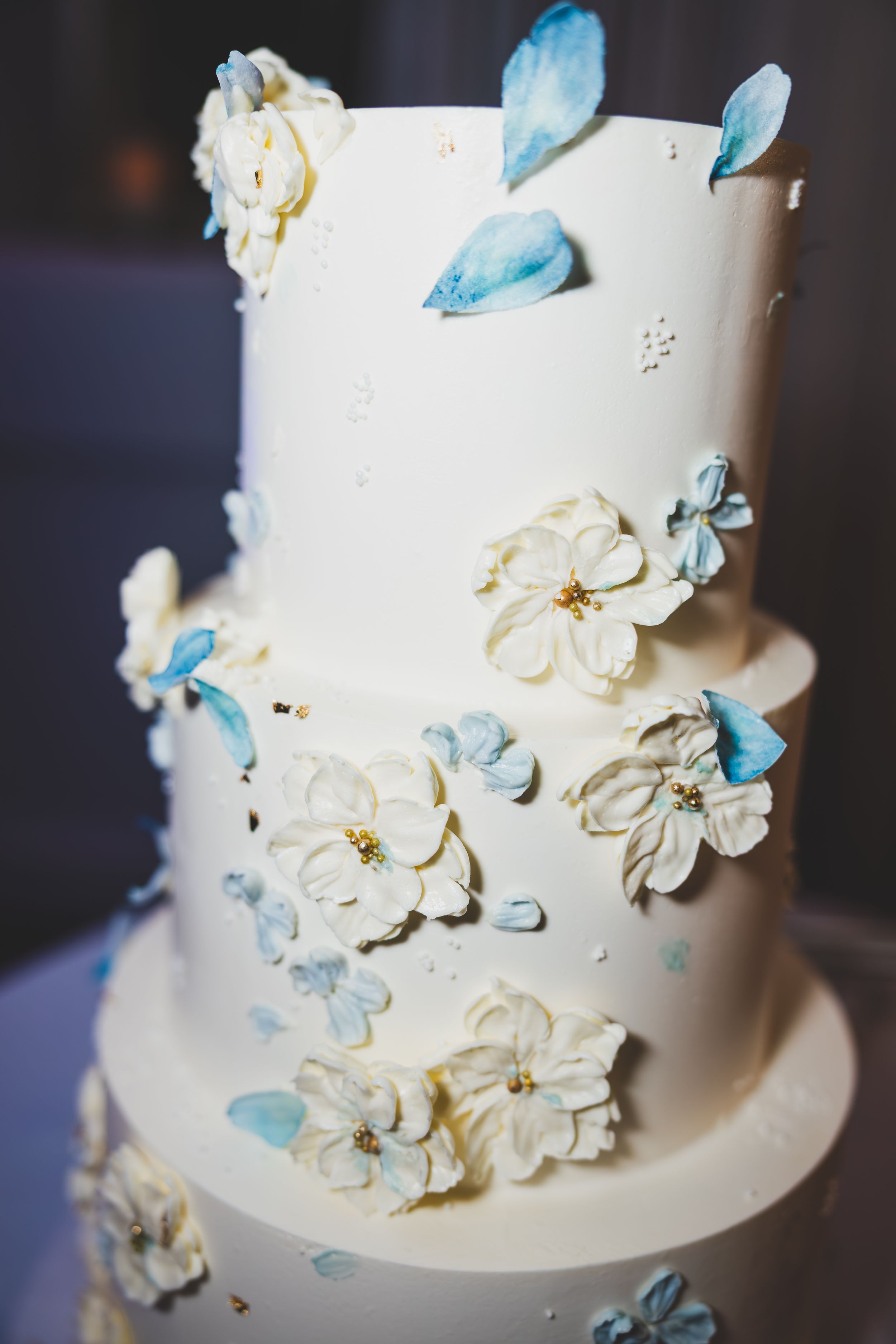 White wedding cake decorated with delicate white sugar flowers and light blue butterflies cascading down the tiers.