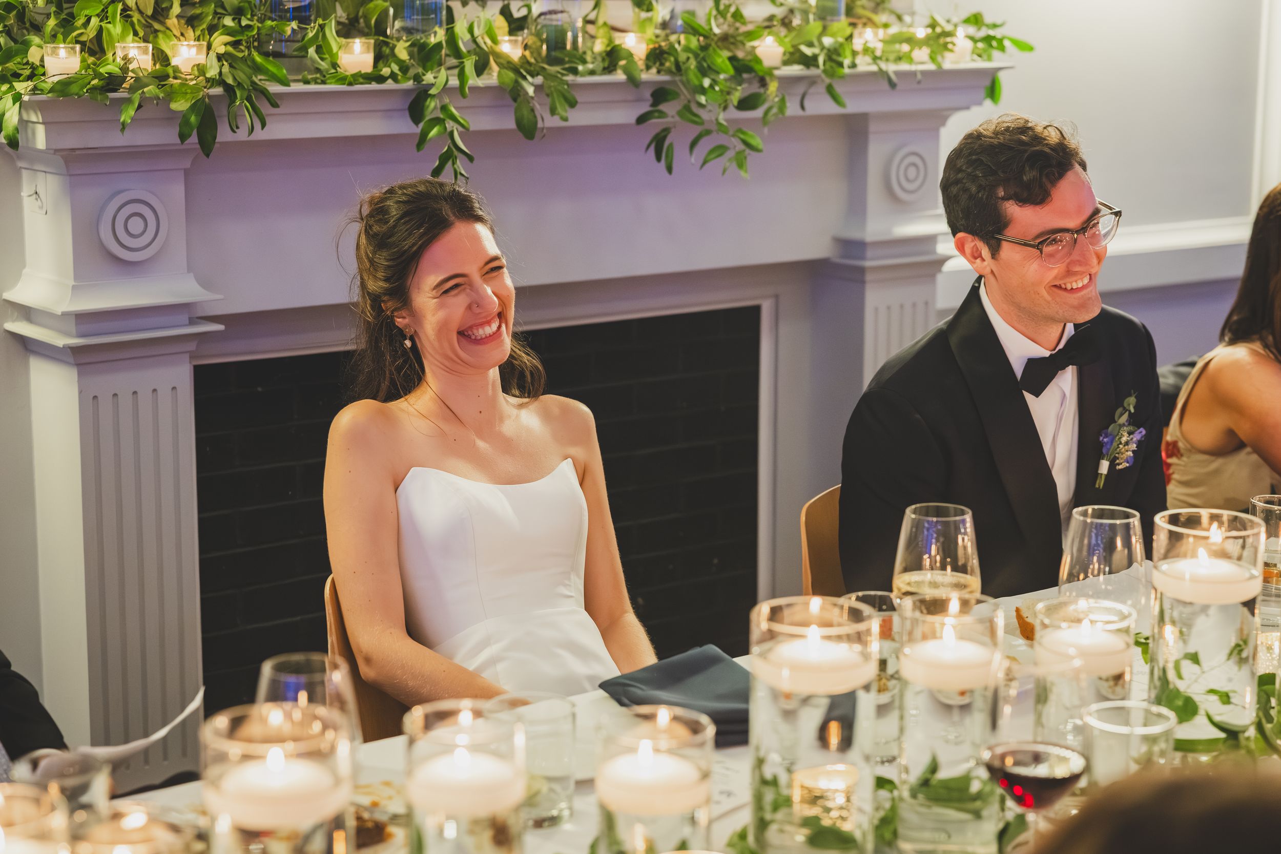 Elegant wedding reception table setting with white linens, floral centerpieces and glowing candles in a formal dining room.