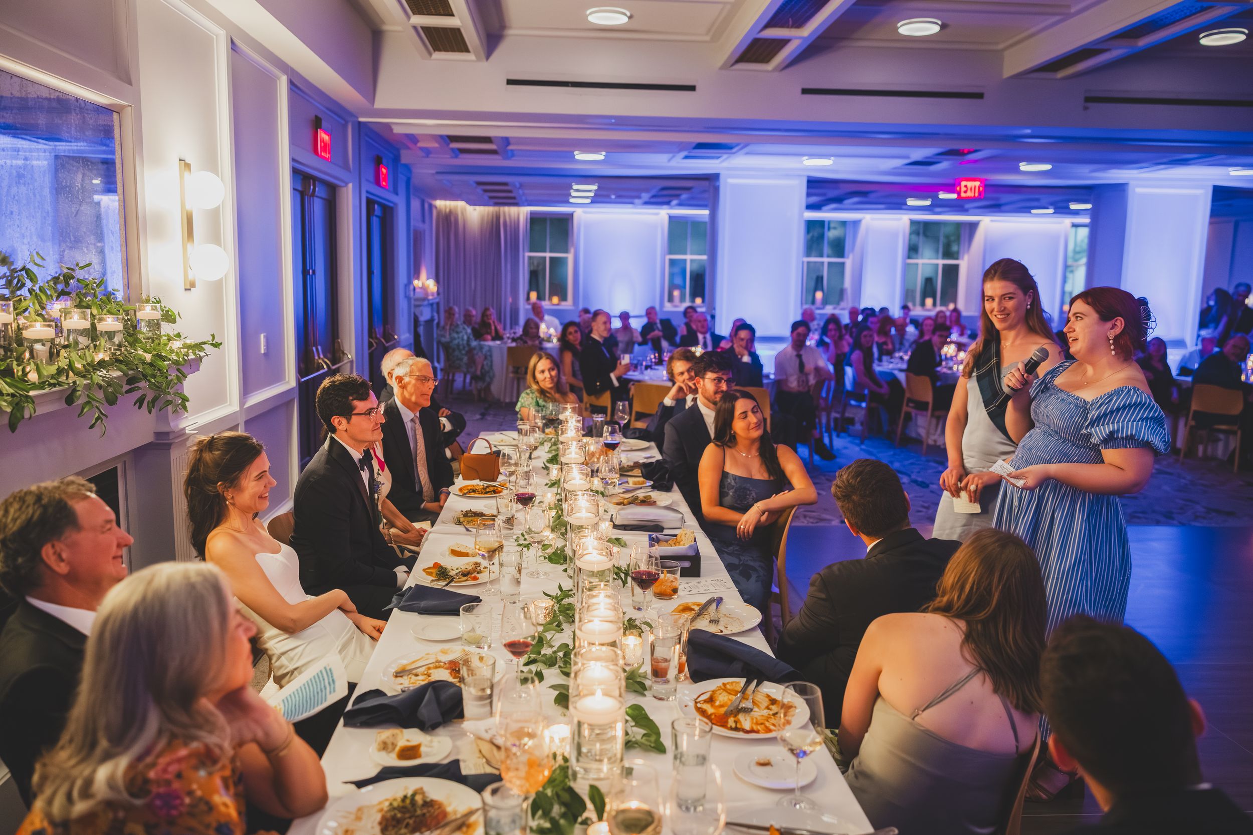 Wedding guests enjoy an elegant reception dinner at long tables decorated with floral centerpieces and soft lighting.
