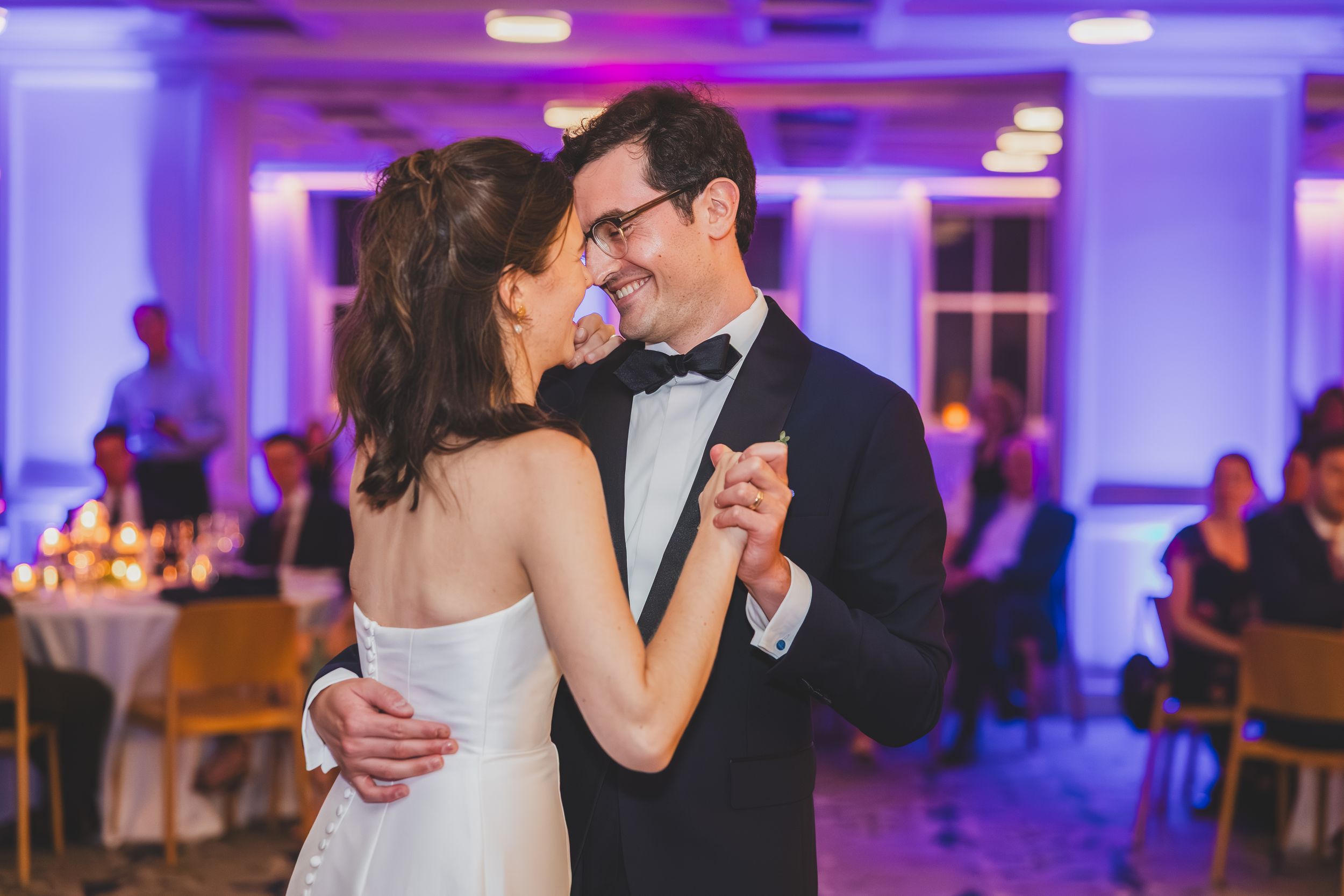 A couple shares an intimate dance moment at their wedding reception with purple lighting in the background.
