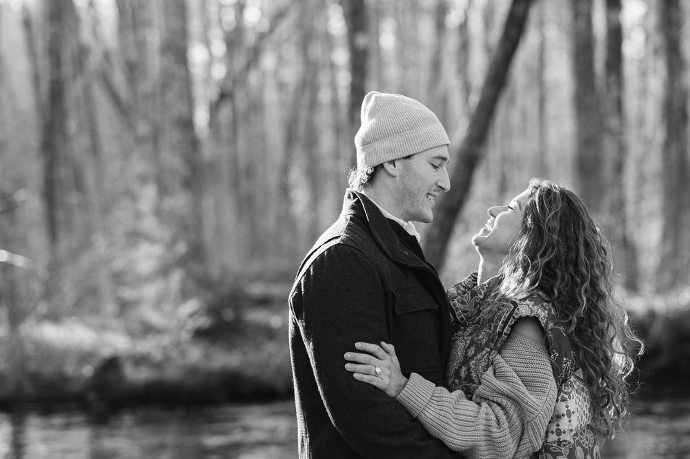 A couple embraces in a romantic moment outdoors in a wooded setting during a black and white photo session.