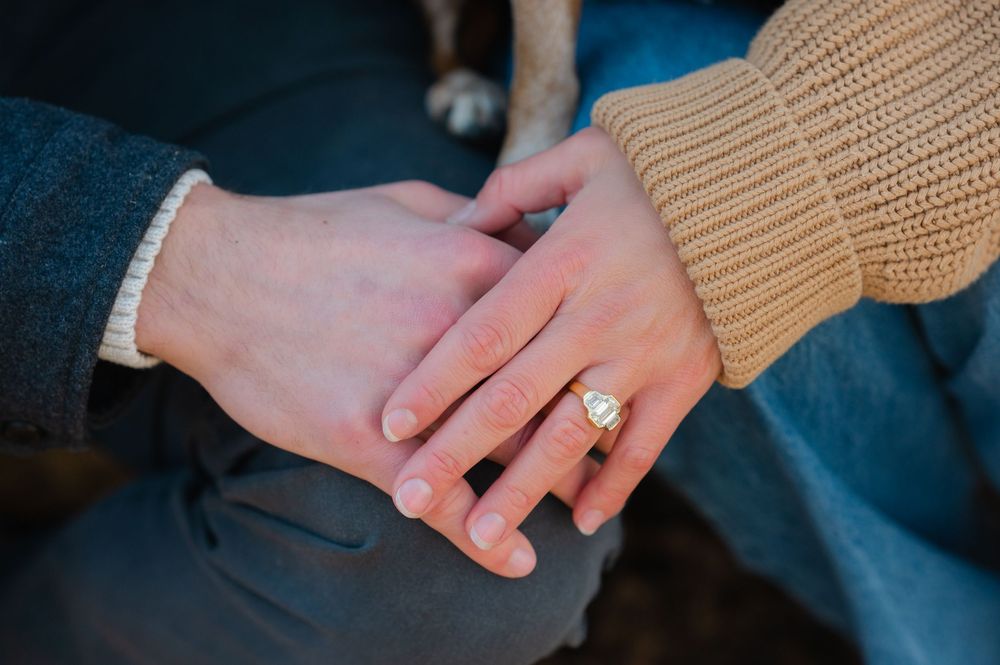 Close-up of hands with an engagement ring resting on blue denim fabric.
