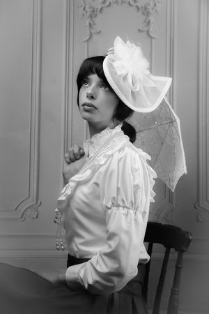 Black and white photo of a girl in a Victorian, edwardian dress - holding a parasol, and a regency hat - looking up to the left
