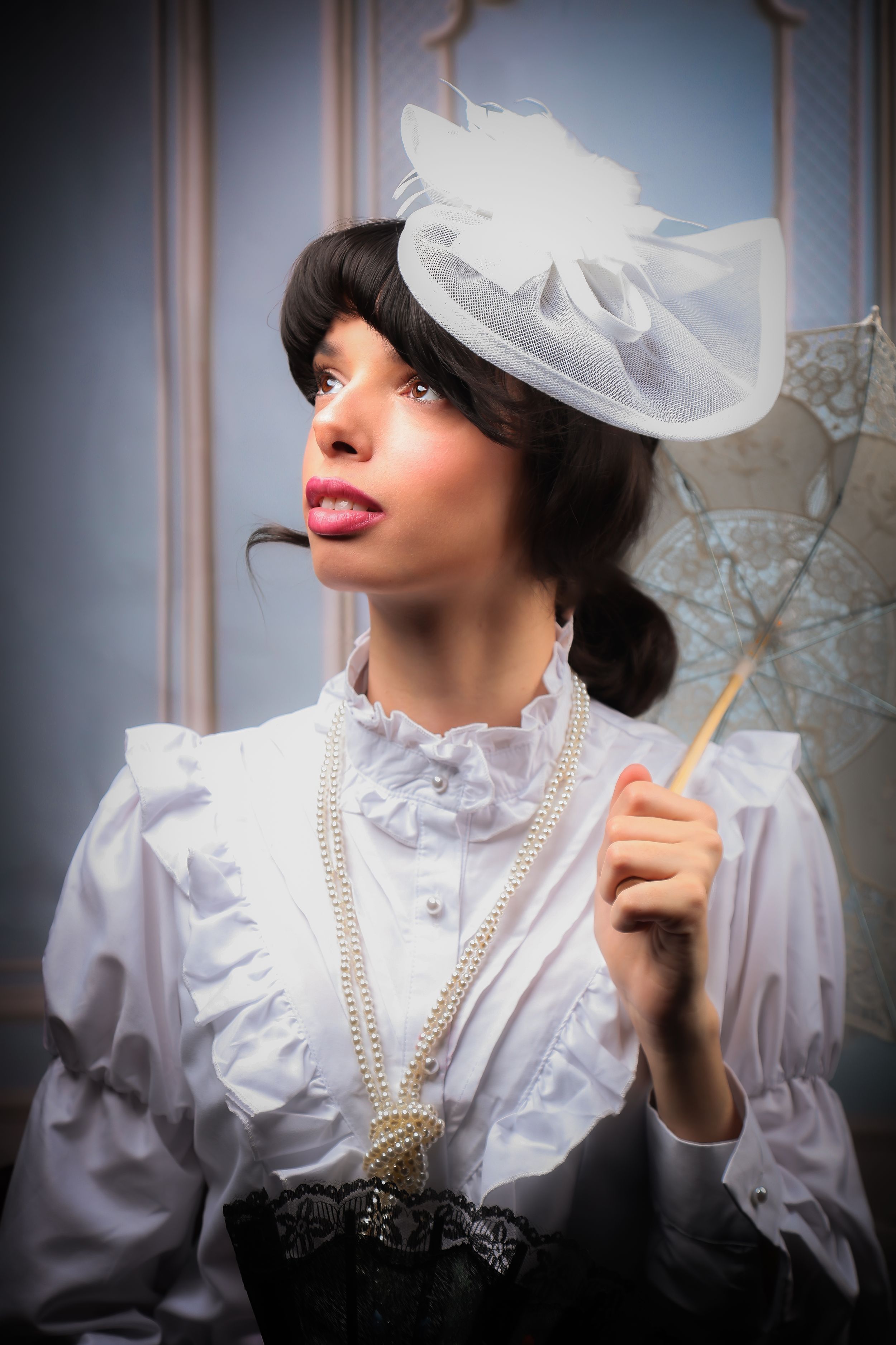 A girl in a Victorian, edwardian dress - holding a parasol and a regency hat, looking up to the left of the photograph
