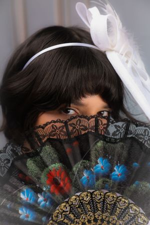 Photo of a girl close up, holding a fan to her face and wearing a regency hat, looking straight to the camera