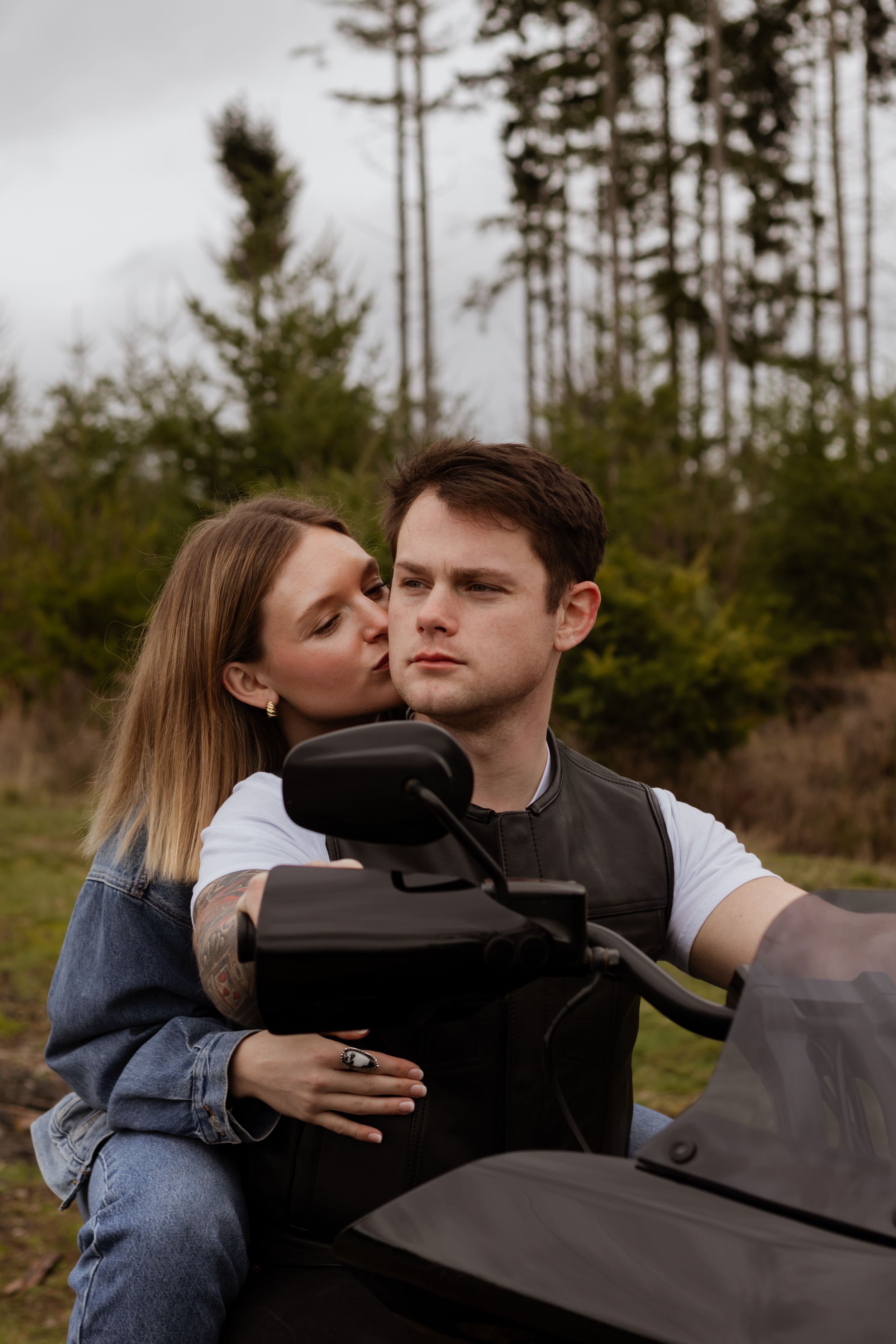 Woman kissing a man on the cheek while embracing him from behind on a black motorcycle during photoshoot in yelm wa with local photographer