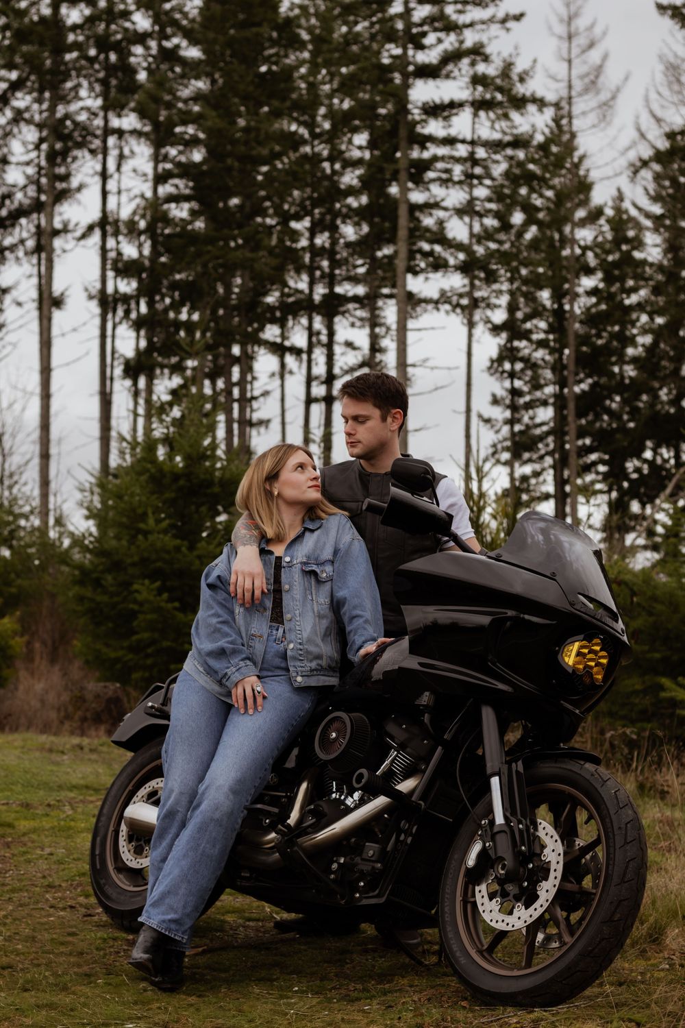 Couple leaning against a black motorcycle surrounded by tall pine trees in yellm washington taken by pierce county photographer