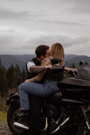 Couple sharing a passionate kiss while sitting together on a black motorcycle with mountain views behind in Yelm WA with photographer