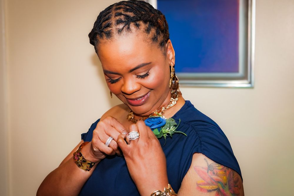 Woman in blue dress pinning a boutonniere, wearing gold jewelry and braided hair at a formal event.