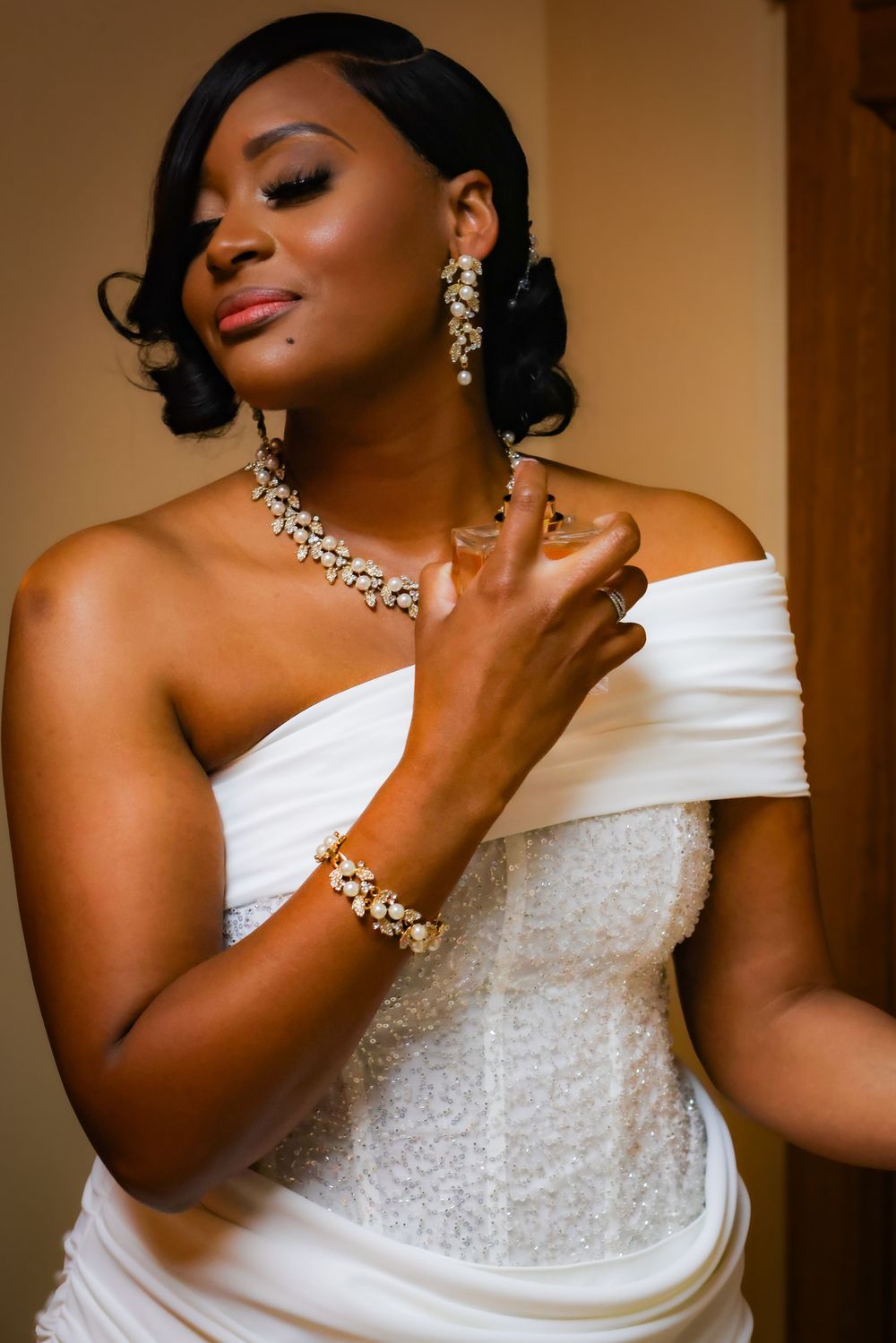 Elegant bride in white strapless gown with gold jewelry, bracelet, and earrings, posing gracefully before her wedding ceremony.