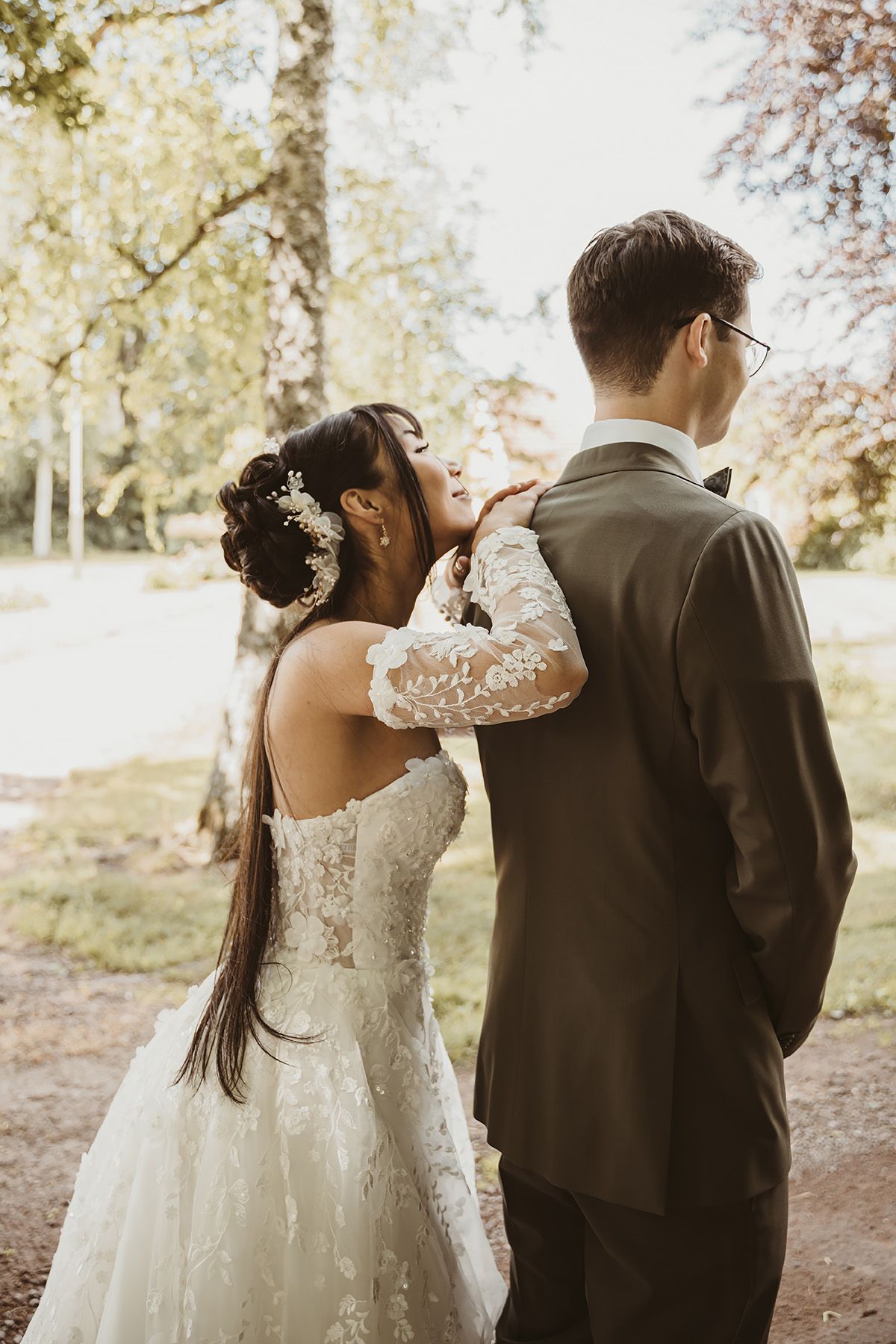 First look fotografering i en vacker allé i Vadstena, brudgummen står med ryggen till och bruden ler och kikar över axeln.