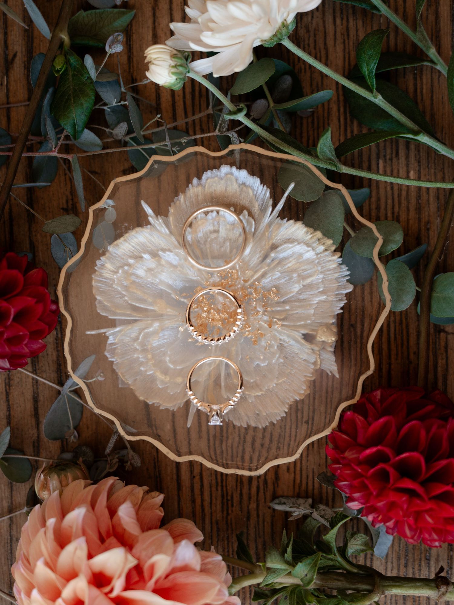 Three gold wedding rings displayed on a dried floral piece surrounded by red and peach flowers.