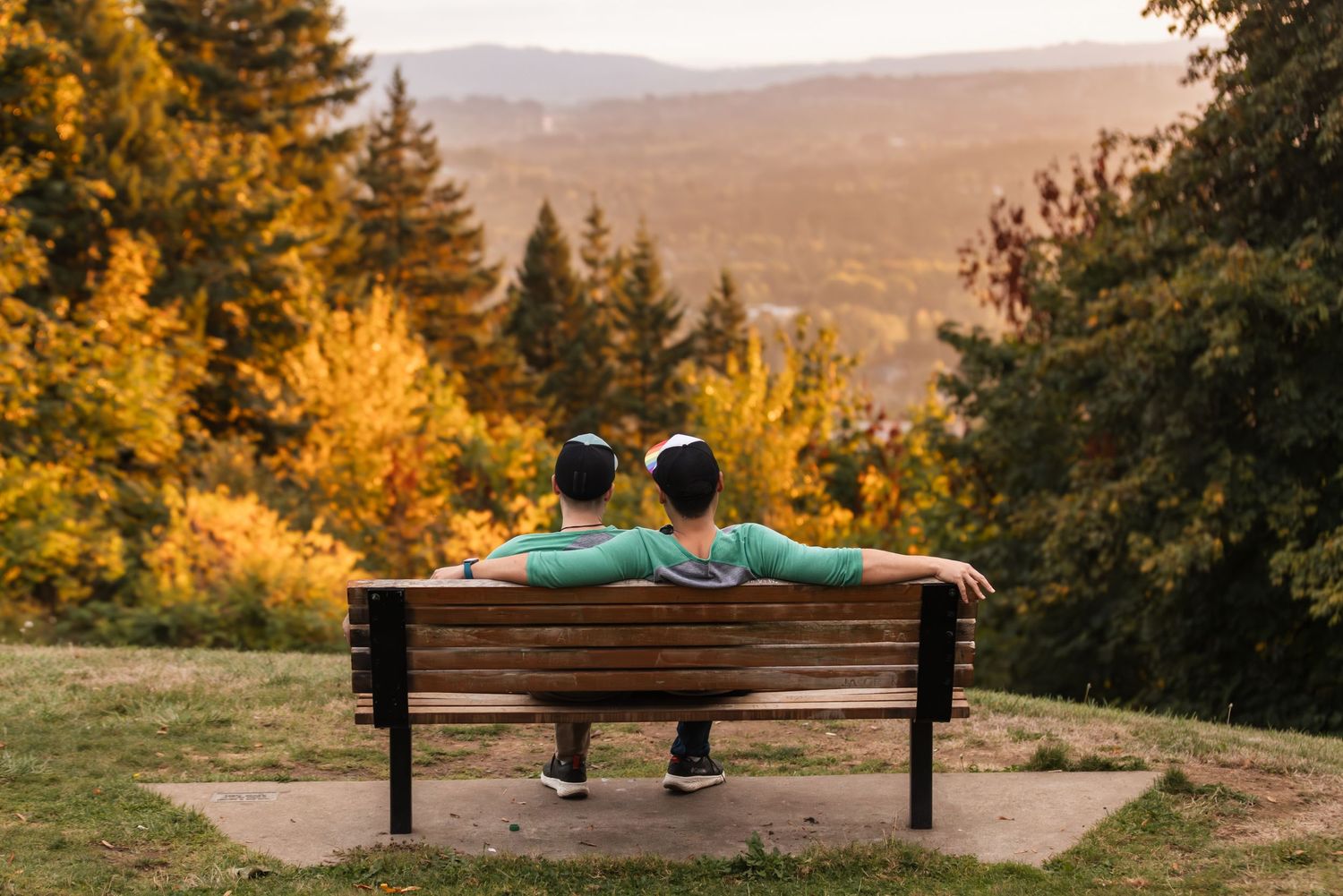 Two people stand together on a wooden viewing platform surrounded by towering redwood trees in a misty forest.